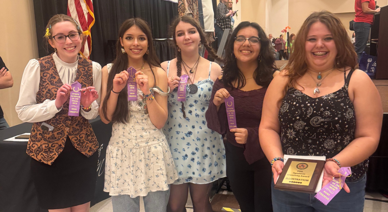 Five students smile in front of a stage holding purple ribbons and a plaque